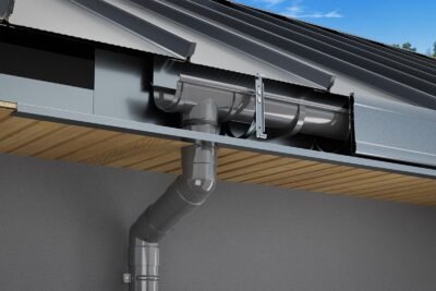 Lietaus nuvedimo sistema: pilka latakas su lietvamzdžiu prie stogo.