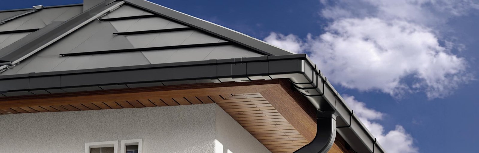 Pilkas stogas su juodais latakais ir lietvamzdžiais mėlyno dangaus fone