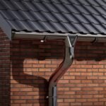 Stačiakampė plieninė lietaus nuvedimo sistema ant raudonų plytų sienos. Lietvamzdis ir latakas.