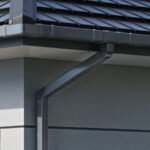 Stačiakampė plieninė lietaus nuvedimo sistema, 135/90 mm, ant namo fasado. Pilkos spalvos latakas ir lietvamzdis.